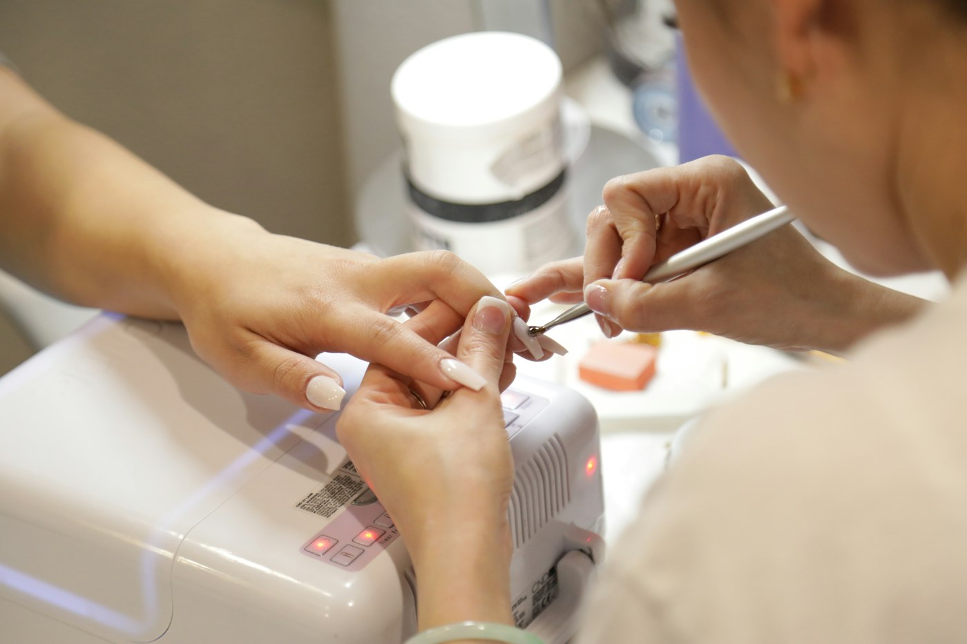 A nail technician shaping a client's nails under a lamp